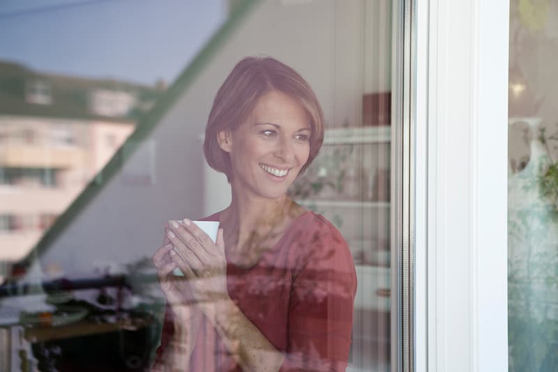 smiling-woman-holding-cup-looking-out-of-window